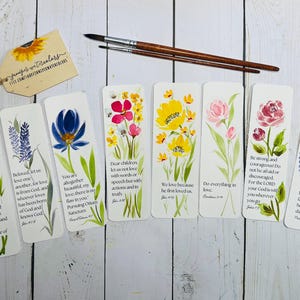 Könnte beinhalten: Aquarell-Lesezeichen mit Blumenmotiven und inspirierenden Zitaten. Jedes Lesezeichen zeigt ein anderes Blumendesign in Rot-, Gelb-, Rosa- und Blautönen mit grünen Blättern. Der Text enthält Bibelverse.