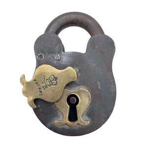 May include: An antique padlock with a dark grey, weathered body and a brass keyhole cover. The cover is marked with "Patent" and a crown emblem. The shackle is dark, rounded metal. A vintage security item.