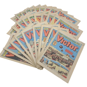 Puede incluir: Una colección de cómics vintage con el título "Victor" en la portada. Los cómics son de varios tonos de azul, rojo y amarillo. Los cómics están dispuestos en forma de abanico, con el cómic superior siendo el más visible.