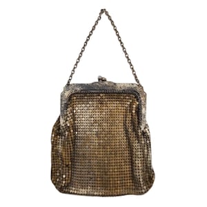 May include: A vintage gold-toned metal mesh handbag with a chain handle. The bag has a rectangular shape with a clasp closure and a textured, shimmering surface. The chain is a darker, antique metal.