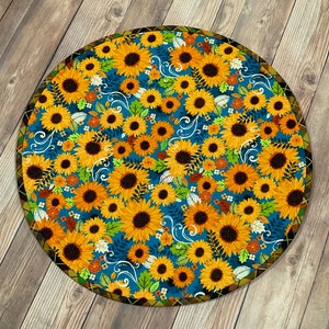 May include: A round blue and yellow rug with a floral pattern of sunflowers. The rug has a brown border with a decorative pattern.