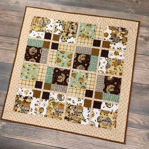 May include: A patchwork quilt with a brown, green, and white color scheme. The quilt is made up of squares with different patterns, including pumpkins, leaves, and flowers. The quilt is edged with a brown trim.