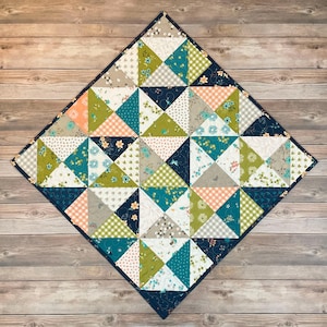 May include: A handmade quilt with a diamond shape, featuring a patchwork design of triangles in various patterns and colors. The quilt includes floral, gingham, and solid fabrics in shades of teal, green, peach, and navy blue. The quilt is approximately 30 inches by 30 inches.