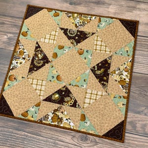 May include: A brown, green, and beige patchwork quilt with a geometric pattern. The quilt is made of various fabrics with different prints, including owls, pumpkins, and plaid.