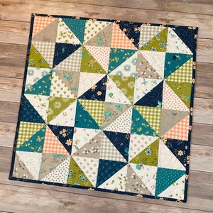 May include: A patchwork quilt with a geometric design. The quilt features triangles in various patterns, including floral, gingham, and solid colors. The color palette includes teal, green, peach, gray, and navy blue. The quilt is bordered with a navy blue fabric.