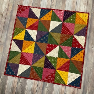 Pode incluir: Uma colcha de retalhos com uma variedade de cores e padrões, incluindo vermelho, verde, amarelo e azul. A colcha é feita de pequenos quadrados e triângulos, e tem um design simples e geométrico.