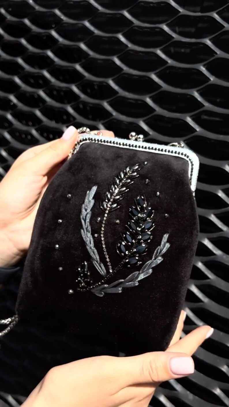 May include: A black velvet evening bag with a silver chain strap and a floral design embroidered with black and silver beads.