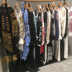 May include: A rack of embroidered shirts with various colorful patterns and designs. The shirts are all long-sleeved and have a traditional Ukrainian style.