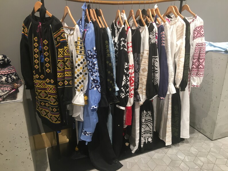 May include: A rack of embroidered shirts with various colorful patterns and designs. The shirts are all long-sleeved and have a traditional Ukrainian style.