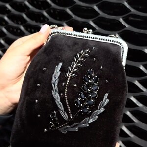 May include: A black velvet evening bag with a silver chain strap and a floral design embroidered with black and silver beads.