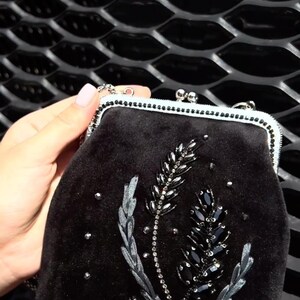 May include: A black velvet clutch bag with a floral design embroidered with black beads and sequins.