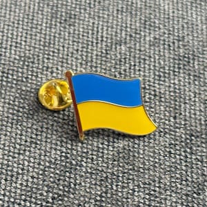 May include: A gold-colored pin with a blue and yellow Ukrainian flag design.
