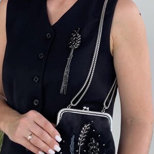May include: A black velvet evening bag with a silver chain strap and a beaded floral design. The bag has a silver clasp and a black tassel.