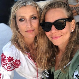 May include: Two women are smiling for a selfie. The woman on the left is wearing a white embroidered blouse with red accents. The woman on the right is wearing a green shirt with black and white embroidery and black sunglasses.