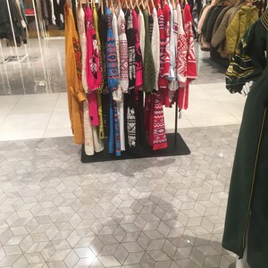 May include: A rack of colorful embroidered shirts with geometric patterns. The shirts are hanging on a metal rack in a store.
