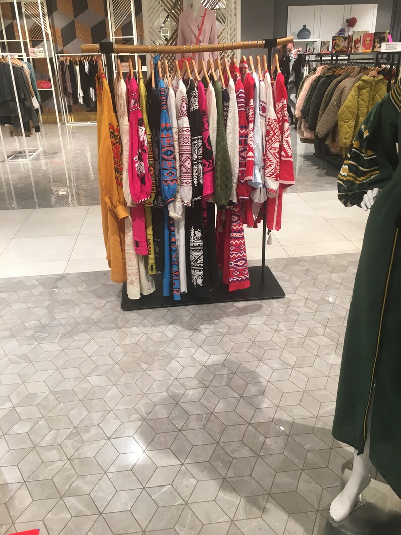 May include: A rack of colorful embroidered shirts with geometric patterns. The shirts are hanging on a metal rack in a store.