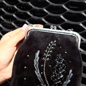 May include: A black velvet clutch bag with a floral design embroidered with black beads and sequins.
