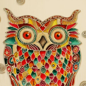 May include: A colorful stained glass owl with intricate details and a gold background. The owl's eyes are large and orange, and its feathers are a mix of red, green, yellow, and blue.