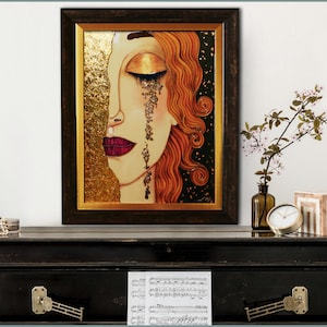 Puede incluir: Una pintura enmarcada de la cara de una mujer con detalles de pan de oro. Sus ojos est&aacute;n cerrados y est&aacute; llorando l&aacute;grimas de oro. El fondo es negro con motas doradas.