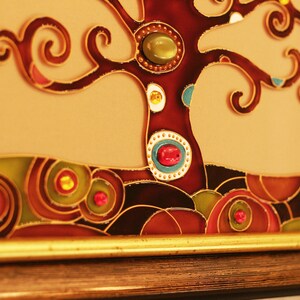 May include: A framed stained glass artwork depicting a stylized tree with brown branches and colorful glass gems. The tree is set against a light brown background with a dark brown border.