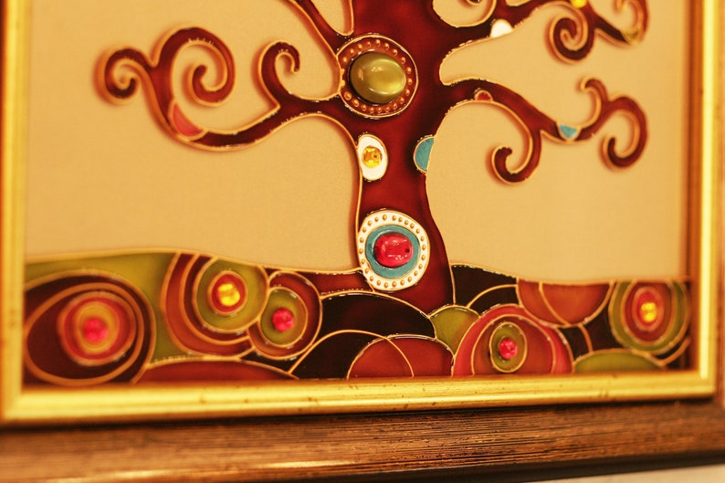 May include: A framed stained glass artwork depicting a stylized tree with brown branches and colorful glass gems. The tree is set against a light brown background with a dark brown border.