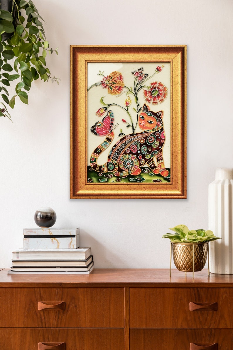 以下が含まれることがあります： カラフルな猫と蝶が描かれたステンドグラスの額縁入りアート作品。猫はピンク、赤、黄色の花に囲まれています。作品は白い背景に飾られています。
