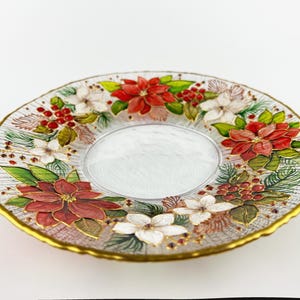 May include: A clear glass plate with a gold rim, decorated with red poinsettias, white flowers, green leaves, and red berries. The center of the plate is a clear, oval shape.