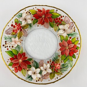 May include: A clear glass decorative plate with a gold rim, featuring a poinsettia and berry design. The plate has a central recessed area and is adorned with red, white, and green floral elements. A festive holiday accent.