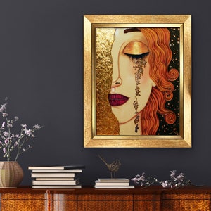 Puede incluir: Una pintura enmarcada de la cara de una mujer con detalles de pan de oro. Sus ojos est&aacute;n cerrados y est&aacute; llorando l&aacute;grimas de oro. El fondo es negro con motas doradas.