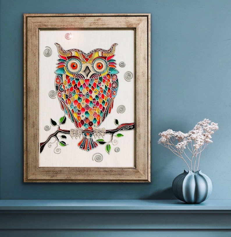 May include: A colorful stained glass owl with intricate details sits on a branch with green leaves. The owl is surrounded by swirls and dots on a white background. The artwork is framed in a light brown wood frame.
