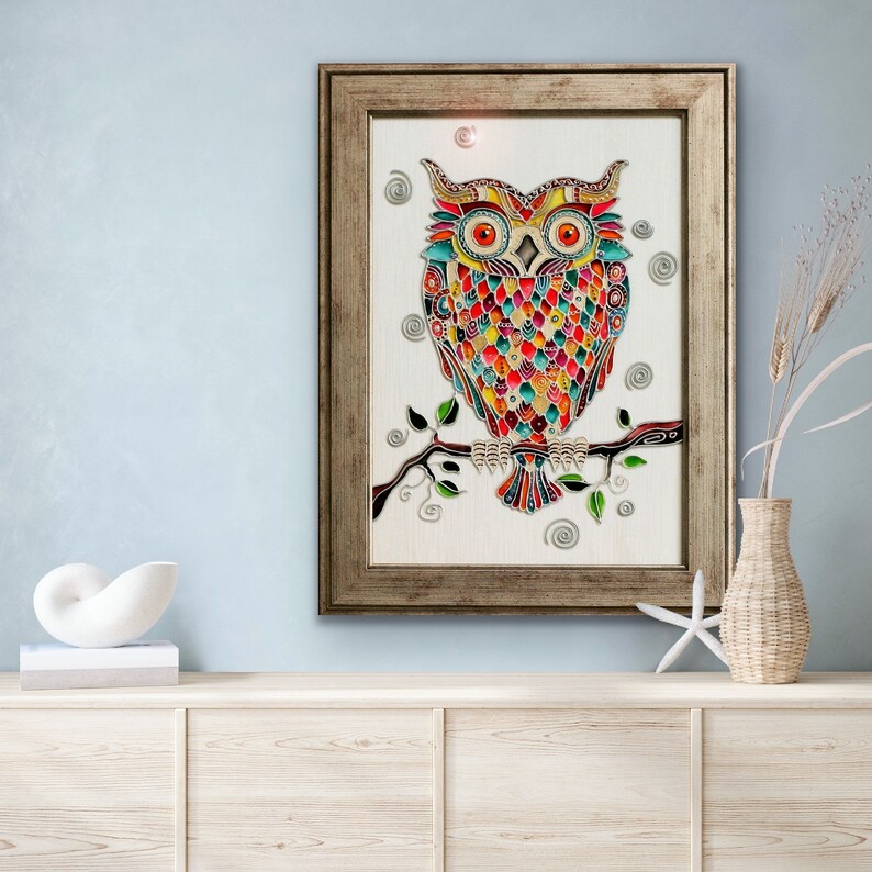 May include: A colorful stained glass owl perched on a branch with green leaves. The owl has red, orange, yellow, green, blue, and purple colors. The background is white.