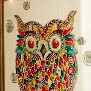 May include: A colorful stained glass owl with red, yellow, green, and blue glass pieces. The owl is framed in a wooden frame.