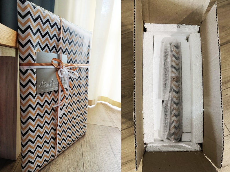 May include: A gift box wrapped in black and orange chevron patterned paper with a white ribbon and a silver gift tag. The box is sitting on a wooden surface. The box is being placed into a larger cardboard box with white styrofoam packing peanuts.