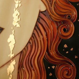 Puede incluir: Primer plano de una obra de arte en vitral que representa el cabello de una mujer. El cabello est&aacute; peinado en una serie de ondas y rizos, con un fondo oscuro y detalles dorados.
