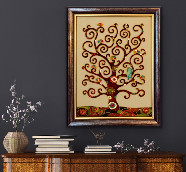 May include: A framed artwork featuring a stylized tree with brown branches and colorful leaves. The tree is set against a cream background with a brown border. The artwork is in a dark brown frame with a gold trim.