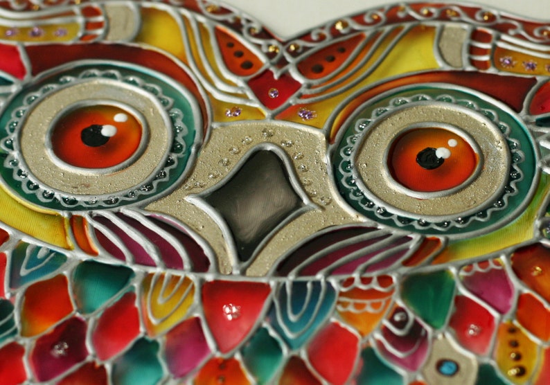 May include: Close-up of a colorful stained glass owl with intricate details. The owl's eyes are large and red with white highlights. The owl's feathers are depicted in shades of red, green, yellow, and blue.
