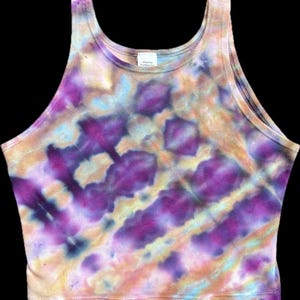 May include: A tie-dye crop top in shades of purple, yellow, and blue. The sleeveless top features a scoop neck and a fitted silhouette. The fabric has a textured appearance, with a pattern of diagonal stripes and irregular shapes.