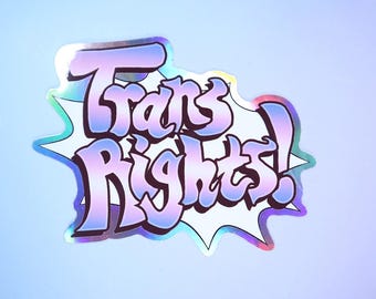 May include: Holographic sticker with the words "Trans Rights!" in a bubble-style font. The text is in shades of purple and blue, with a white outline and a silver holographic effect. The background is a gradient of light blue and purple.