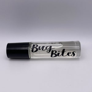 Puede incluir: Un frasco de rodillo de vidrio transparente con una tapa negra. El frasco contiene un líquido transparente y tiene las palabras "Bug Bites" en escritura negra. El frasco está acostado horizontalmente sobre una superficie blanca.