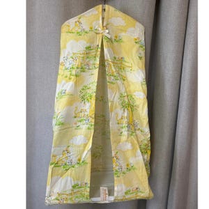 Puede incluir: Un organizador de pañales amarillo y blanco con un estampado de animales lindo. El organizador tiene una solapa que se abre para revelar un bolsillo para guardar pañales. El organizador está hecho de tela y tiene un colgador en la parte superior.