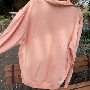 May include: A long-sleeved, peach-colored shirt with a collared neckline. The shirt is made of a soft, lightweight fabric and has a relaxed fit.