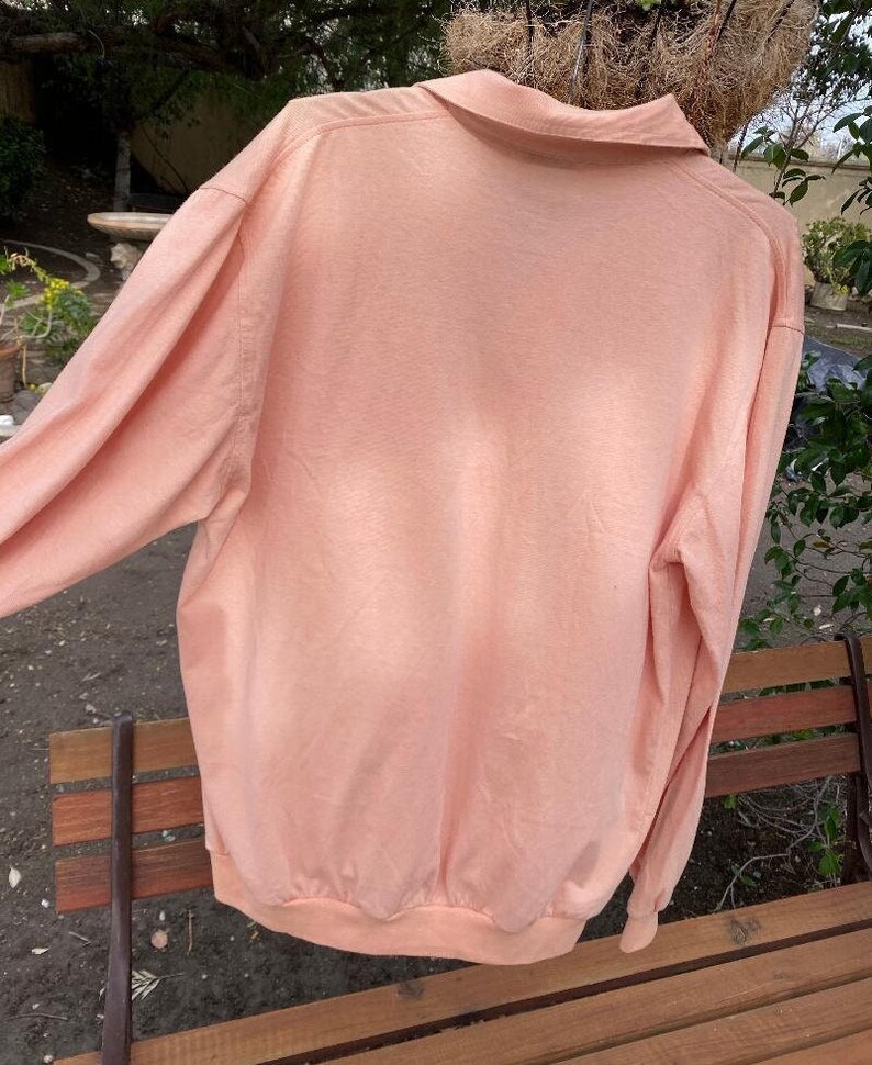 May include: A long-sleeved, peach-colored shirt with a collared neckline. The shirt is made of a soft, lightweight fabric and has a relaxed fit.