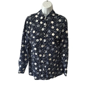 May include: A navy blue button-down shirt with a pattern of white, gray, and light gray polka dots. The long-sleeved shirt has a collared neckline and buttoned cuffs. The shirt is displayed on a white mannequin.