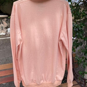 May include: A long-sleeved, light pink collared shirt with a ribbed knit collar and cuffs.