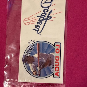 Op de afbeelding: Een witte en blauwe tijdelijke tatoeage met het logo van de Los Angeles Dodgers en een honkballer met de tekst "TO DUCA" en "Jimmy" eronder.
