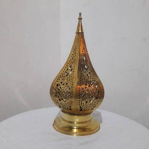 May include: A gold metal lantern with intricate cut-out designs. The lantern has a pointed top and a round base.