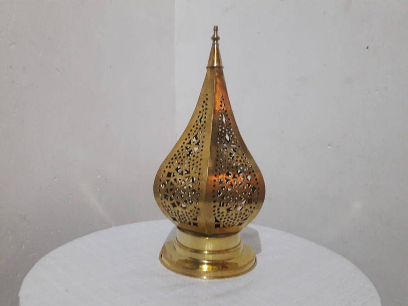 May include: A gold metal lantern with intricate cut-out designs. The lantern has a pointed top and a round base.