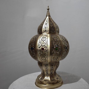 May include: A gold metal lamp with a round, ornate base and a domed top. The lamp has a decorative, cut-out design and features colorful glass accents.