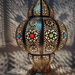 May include: A Moroccan-style table lamp with intricate cut-out designs and colorful glass accents. The lamp is made of metal and has a round base.
