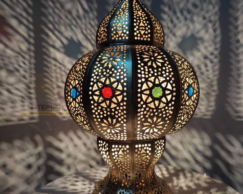 May include: A Moroccan-style table lamp with intricate cut-out designs and colorful glass accents. The lamp is made of metal and has a round base.